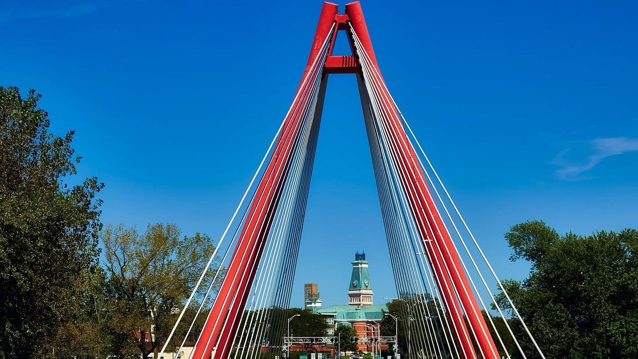 Red cable-stayed bridge carrying the road into downtown Columbus, Indiana, with the county courthouse clock tower ahead