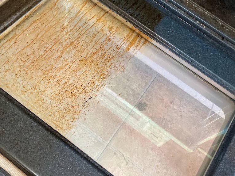 Oven door part-cleaned, showing baked-on residue lifted away